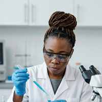 A laboratory scientist in safety glasses pipetting into a rack of test tubes
